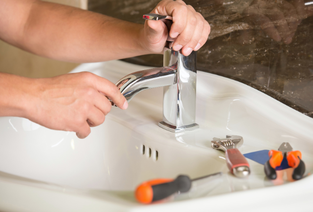 Plumber repairing leaky faucet and sink illustrating emergency plumbing services.