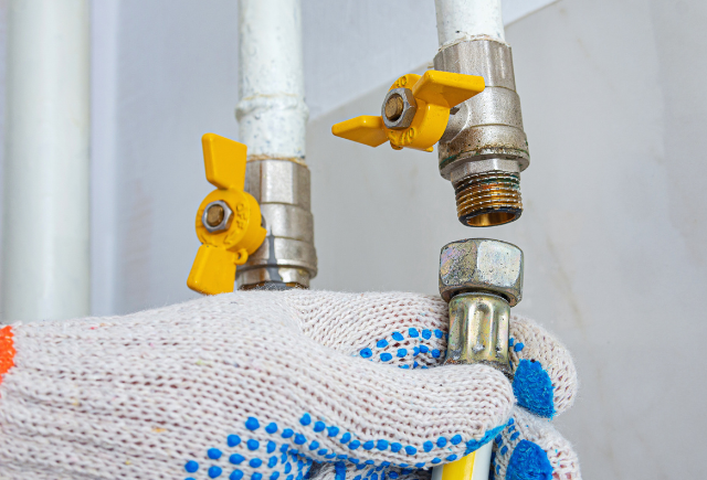 Gas pipes and valves with a gloved hand, illustrating gas leak repair services.