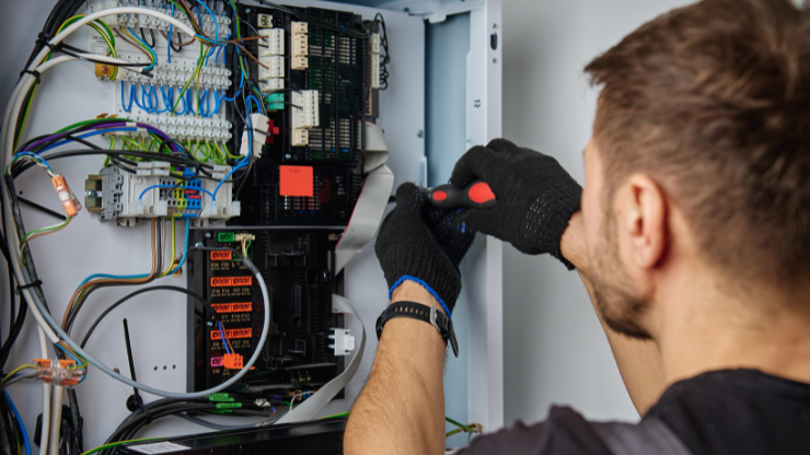 Electrician working on electrical panel with screwdriver, assessing and upgrading home power systems.