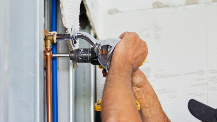 Plumber installing bathroom fixture with drill and copper pipes, full-service plumbing installation.